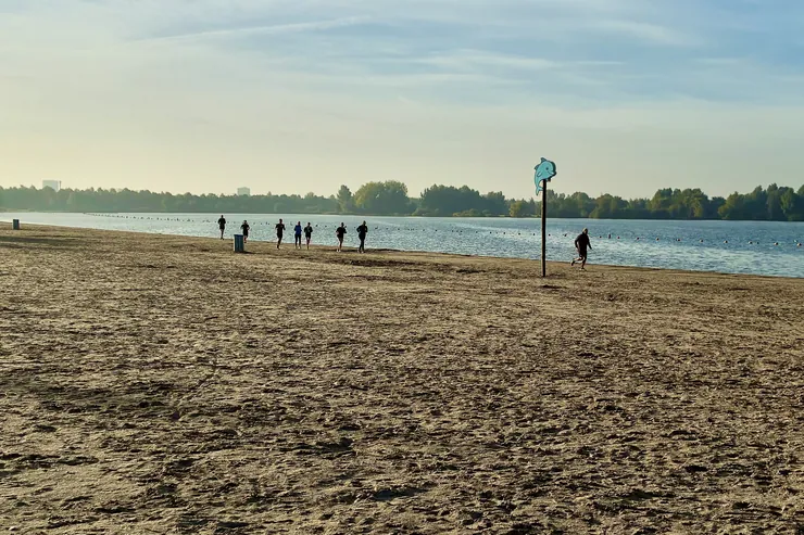 Bootcampgroep loopt in de ochtendzon over het strand van de Haarrijnseplas