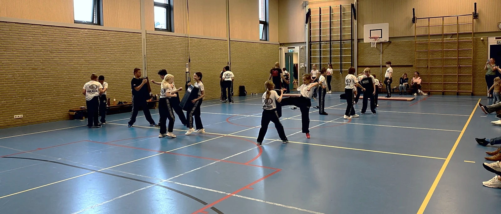 Een les in de gymzaal: tweetallen oefenen terwijl de instructeur rondloopt