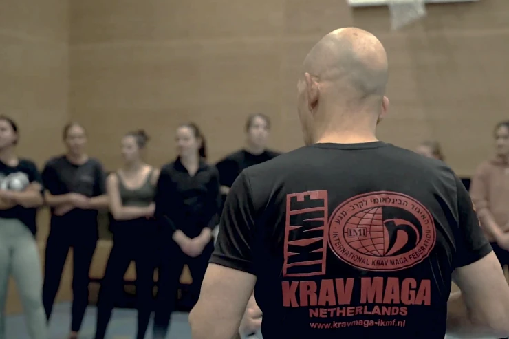 Arik, in zijn IKMF-shirt, staat tegenover een groep vrouwen tijdens de Stay Away workshop